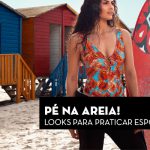Mulher com maiô estampado tropical ao lado de pranchas de surf coloridas na praia.