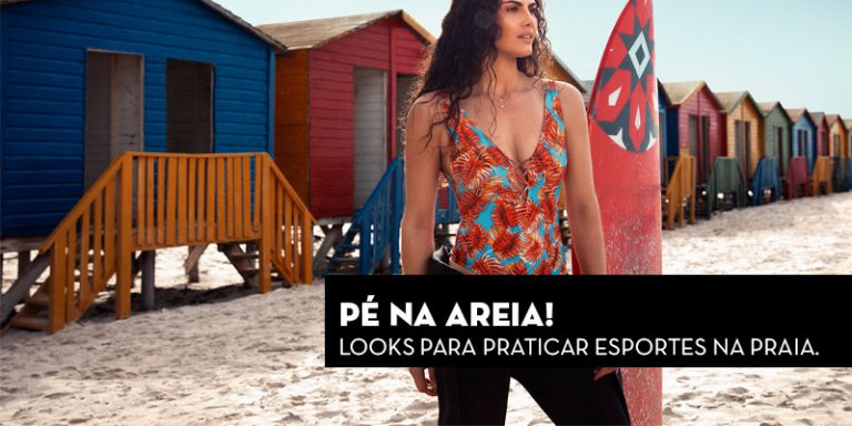 Mulher com maiô estampado tropical ao lado de pranchas de surf coloridas na praia.