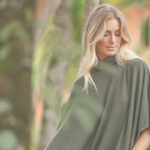 Mulher usando poncho verde em ambiente natural com árvores ao fundo.