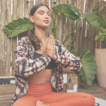 Mulher meditando em ambiente externo, usando jaqueta fitness estampada e legging laranja.