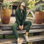 Mulher usando conjunto verde em ambiente natural, sentada em escada de madeira.