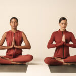 Duas mulheres meditando em tapetes de yoga, vestindo roupas de treino na cor terracota.